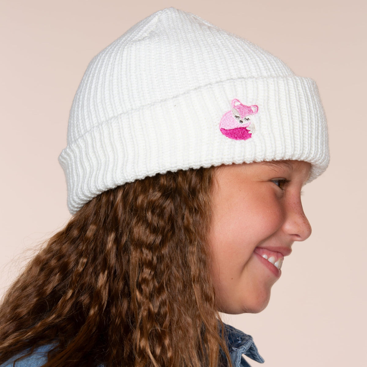 Side view of a white rib-knit beanie with a pink fox patch