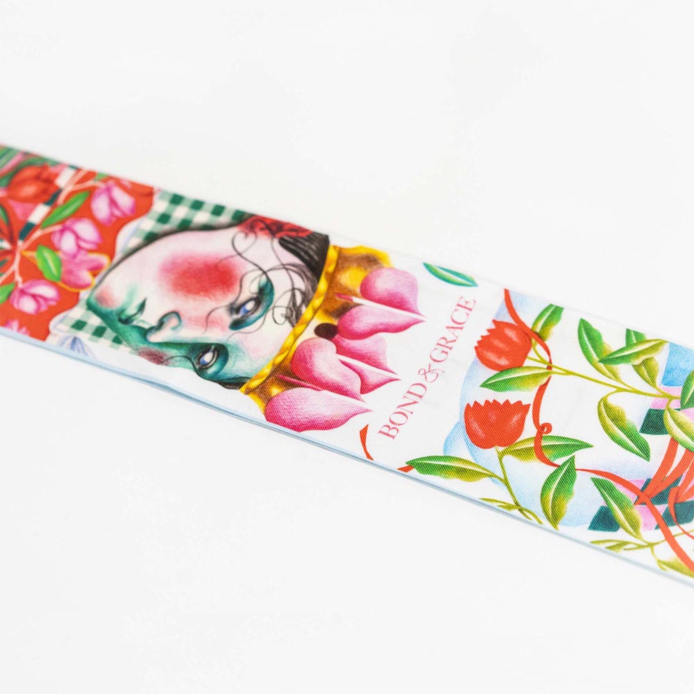 Silk twilly scarf close-up with light blue base, pink flowers, green leaves, and bird