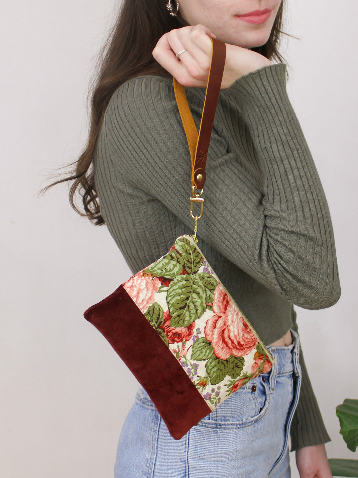 Floral wristlet purse with brown suede bottom, top handle strap, and gold zipper pull.