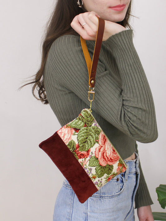 Floral wristlet purse with brown suede bottom, top handle strap, and gold zipper pull.