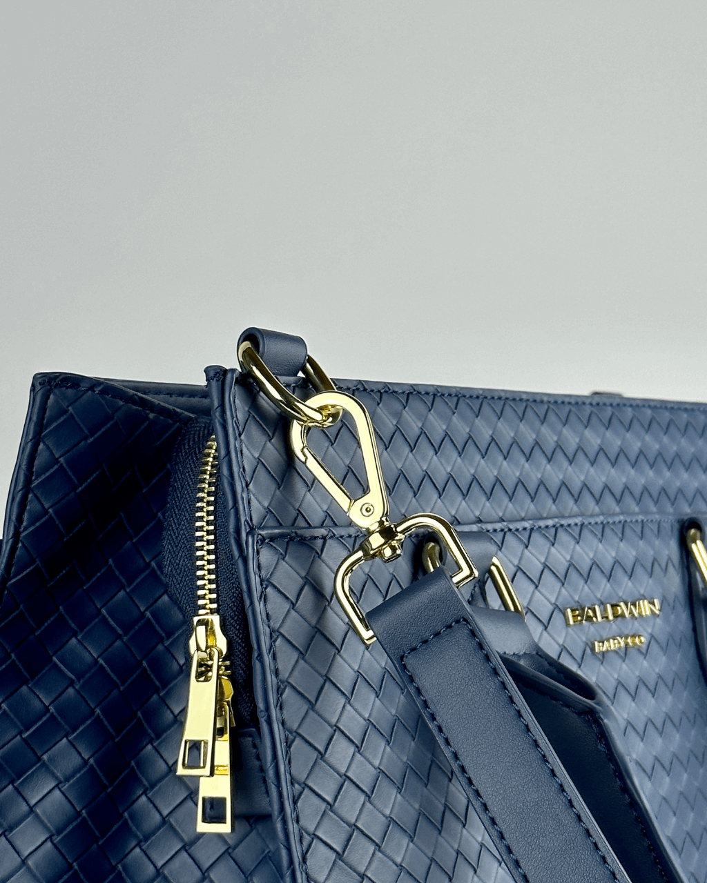 Close-up of the woven tote with gold-tone strap clasp and zipper pulls