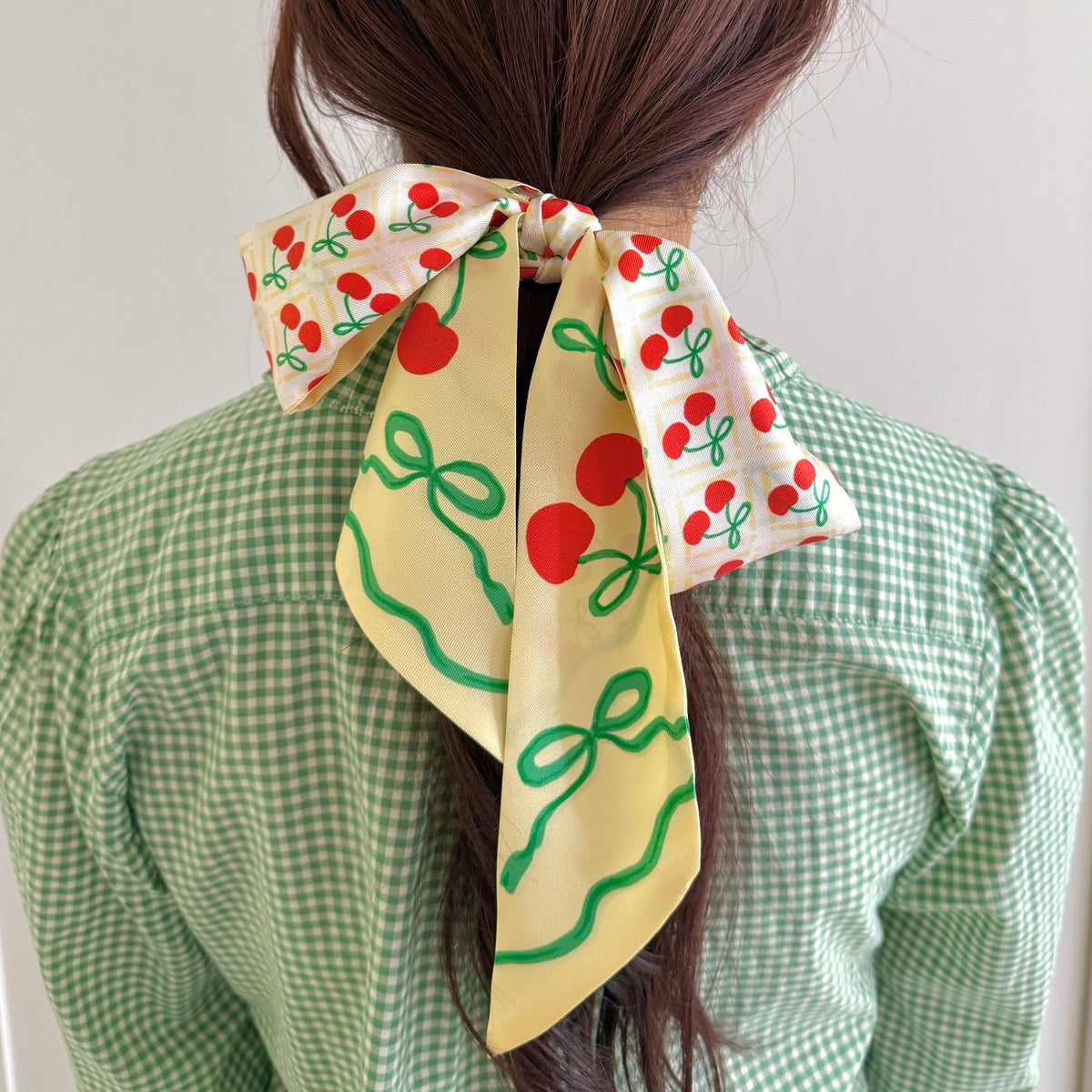 Cherry-pattern ribbon scarf worn in a back bow; cream with red cherries and green stems