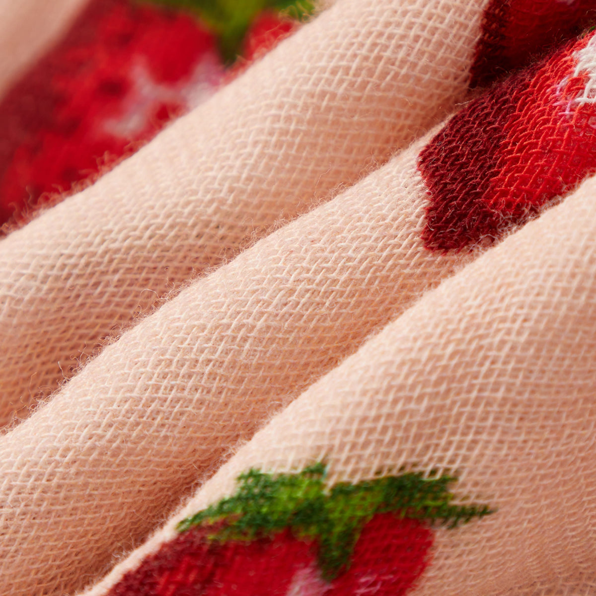 Peach textured towel fabric with red strawberry pattern along stitched edge