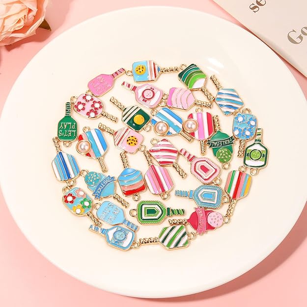 Colorful pickleball jewelry charms with striped, floral, paddle, and ball designs linked by gold-tone chains.