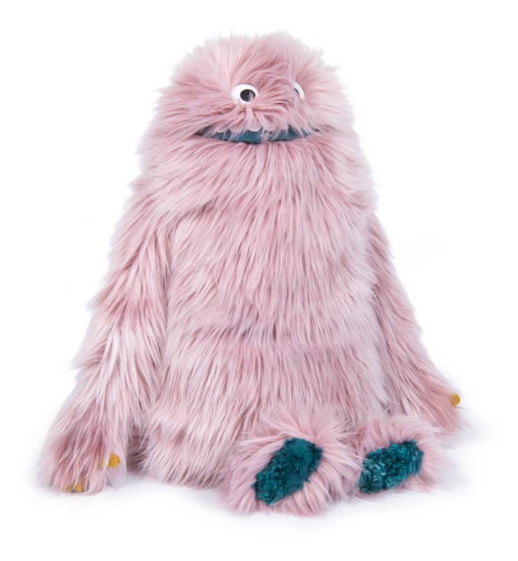Pink fuzzy plush monster with wide eyes, teal belly patch, and small yellow accents.