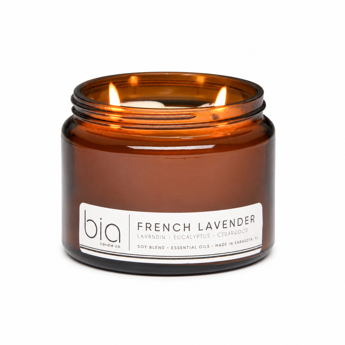 Amber soy candle in glass jar with lit wick, front label and brand visible