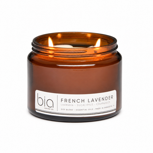 Amber soy candle in glass jar with lit wick, front label and brand visible