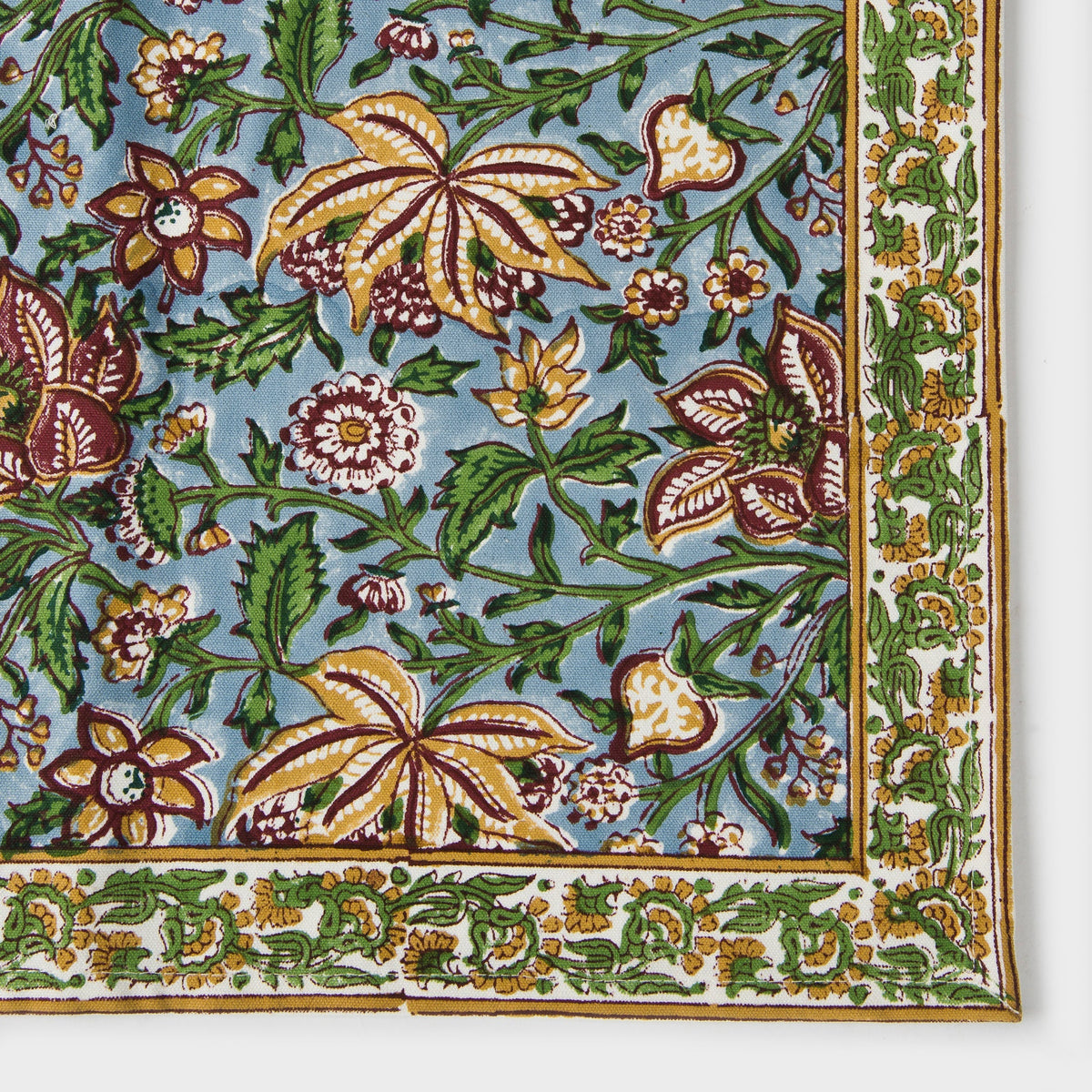 Cotton placemat close-up with green leaves, blue background, and multicolor floral print