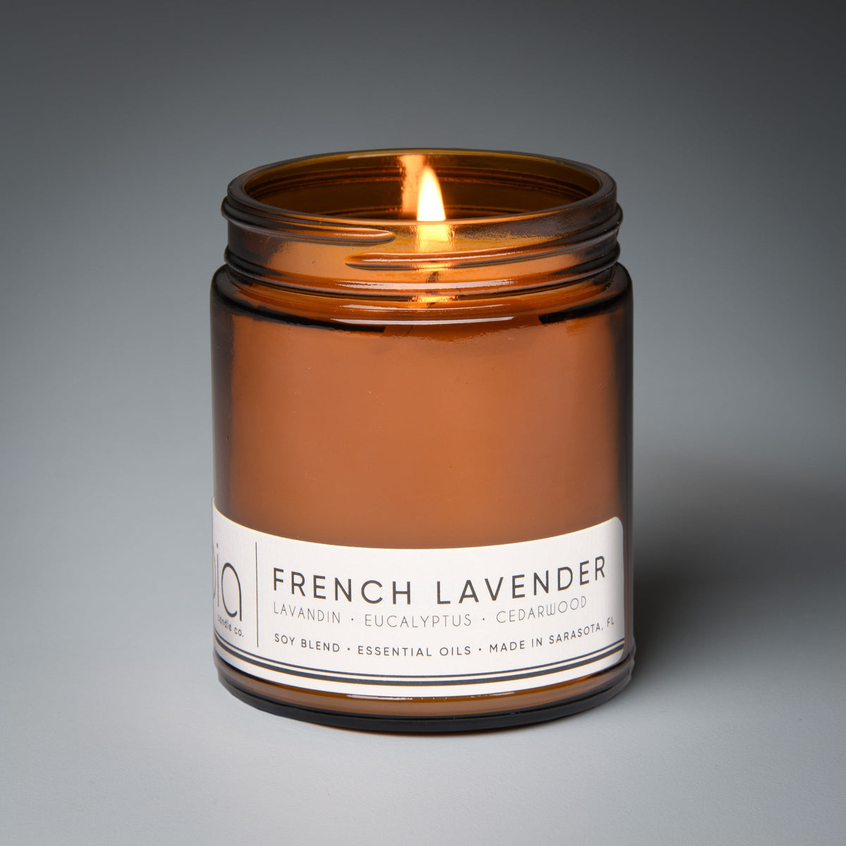 Amber soy candle in glass jar with lit wick, white label around the center
