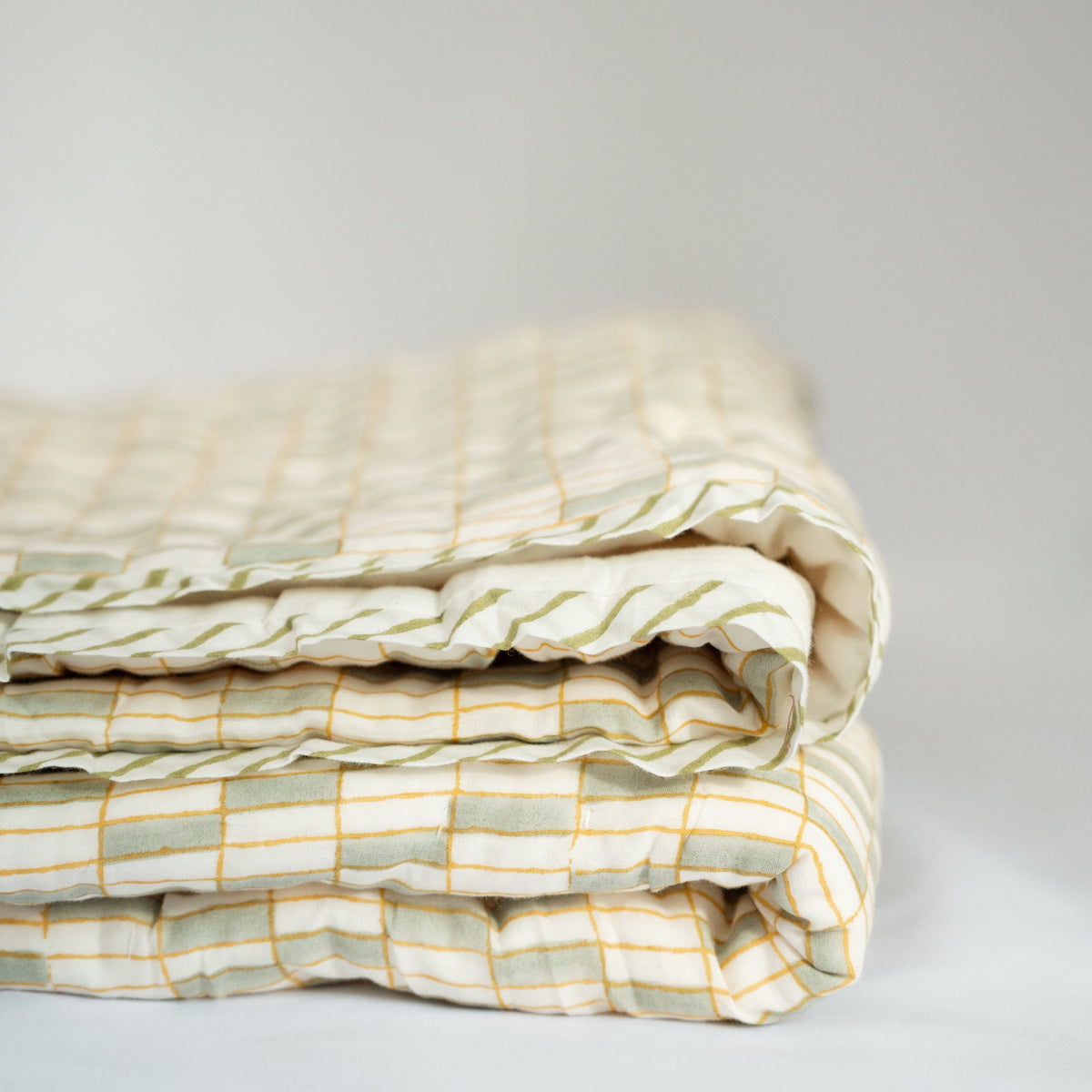Stacked quilt corner with white fabric, green bands, and yellow plaid quilting detail