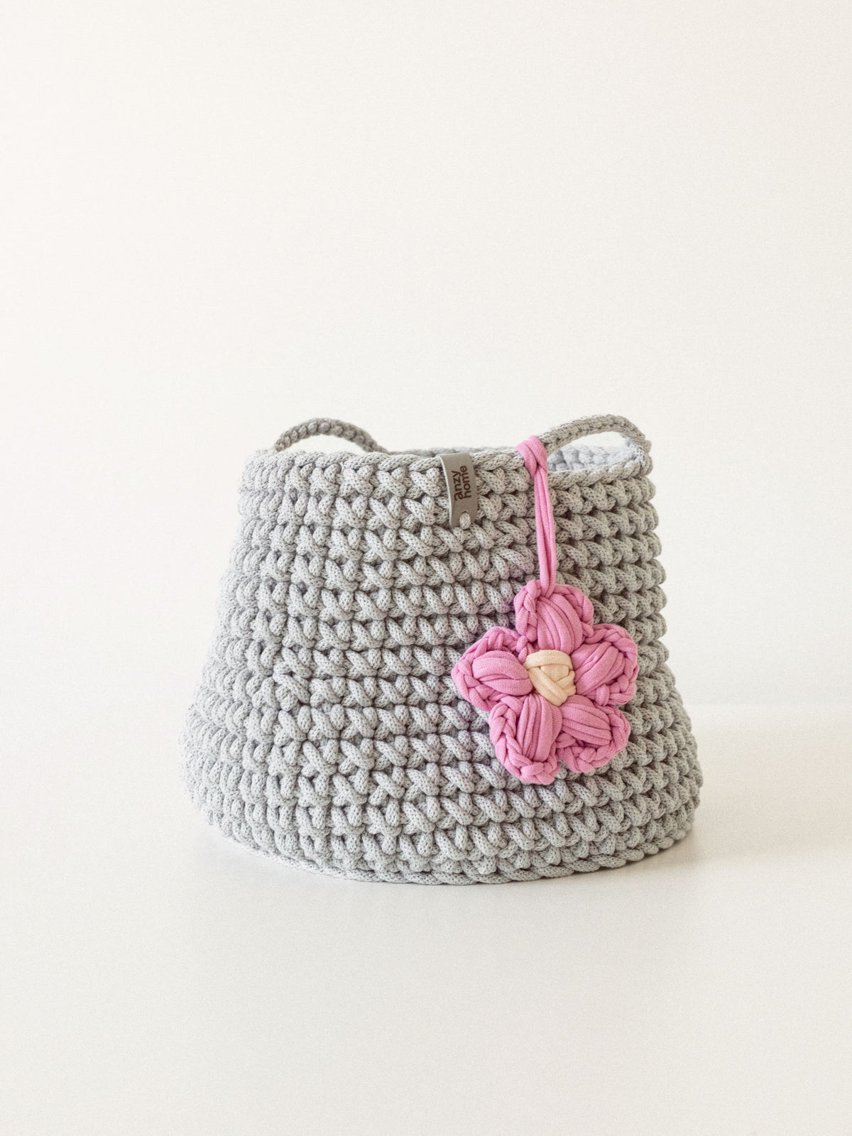 Gray crocheted toy storage basket with loop handle and pink flower charm