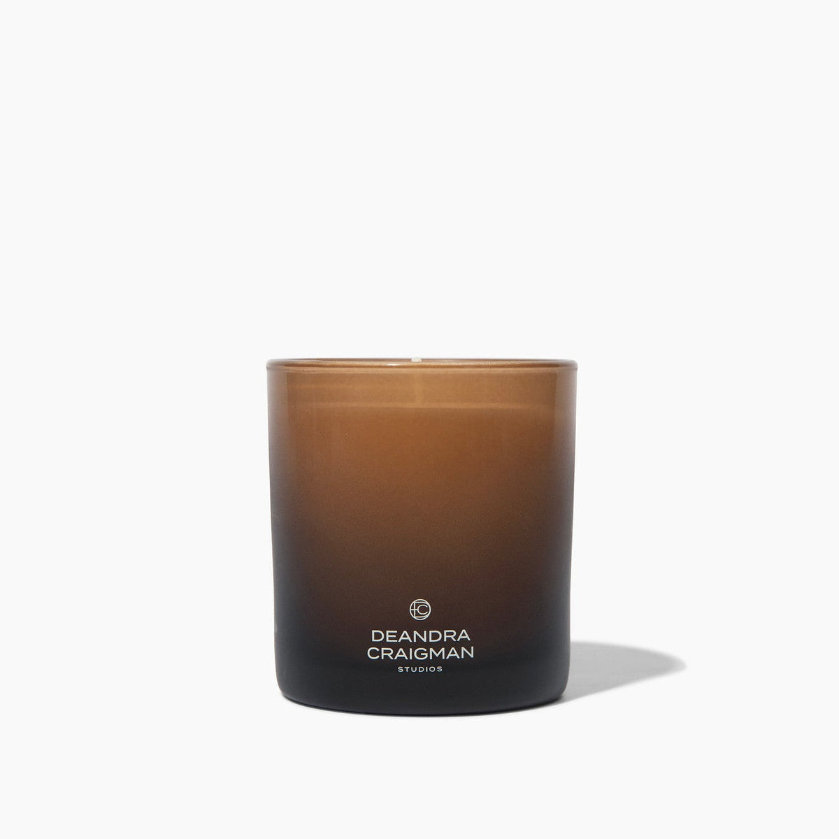 Amber glass jar candle with black base and Deandra Craigman logo, clean studio view