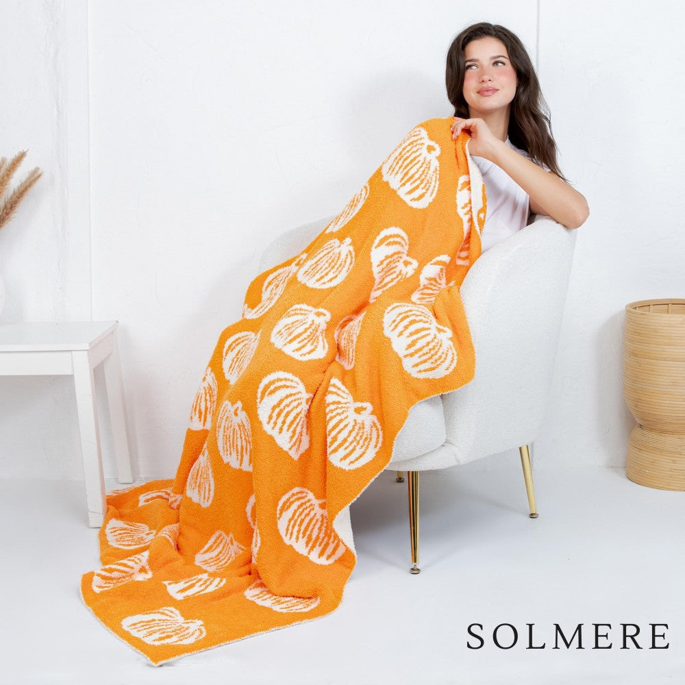 Orange pumpkin-print blanket with white patterns, draped over armchair