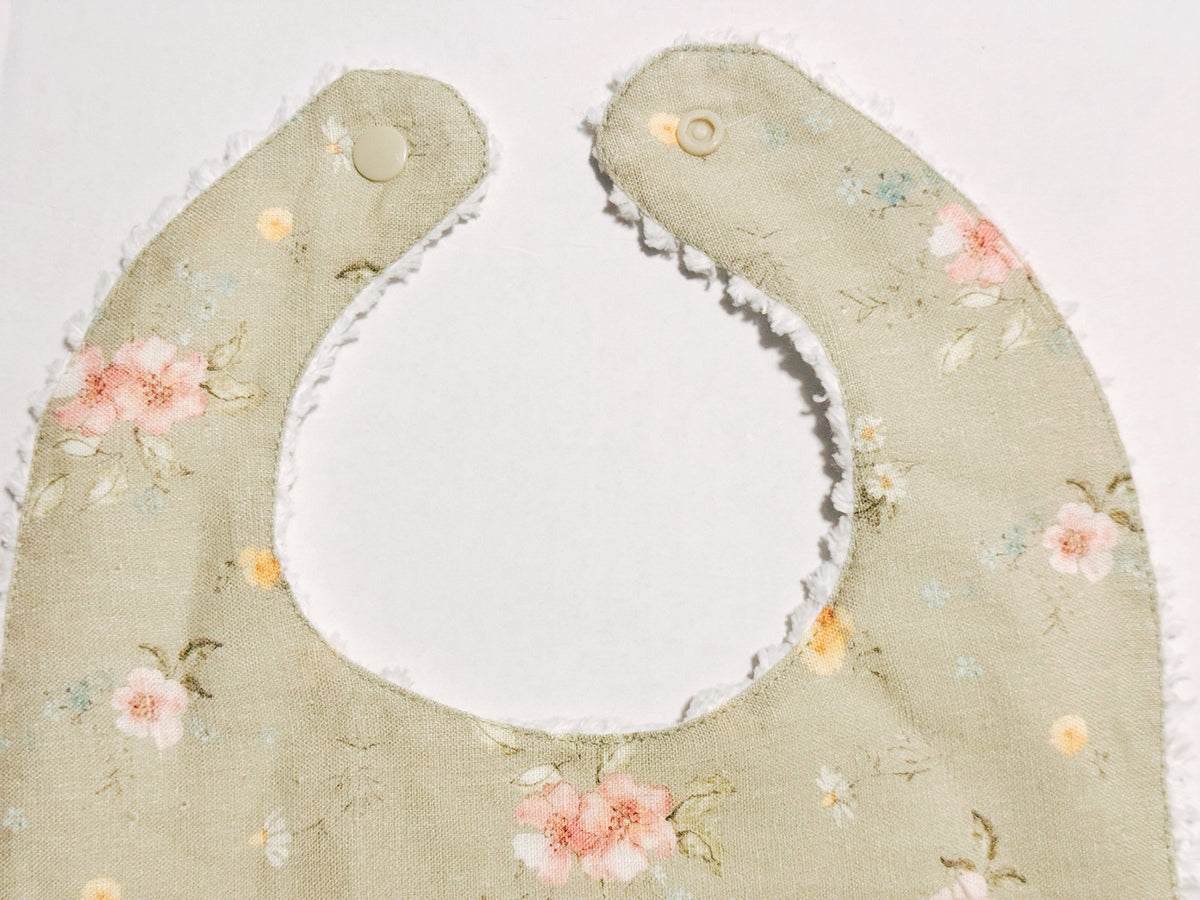 Infant bib close-up: sage floral fabric with rounded neck hole and stitched button tab