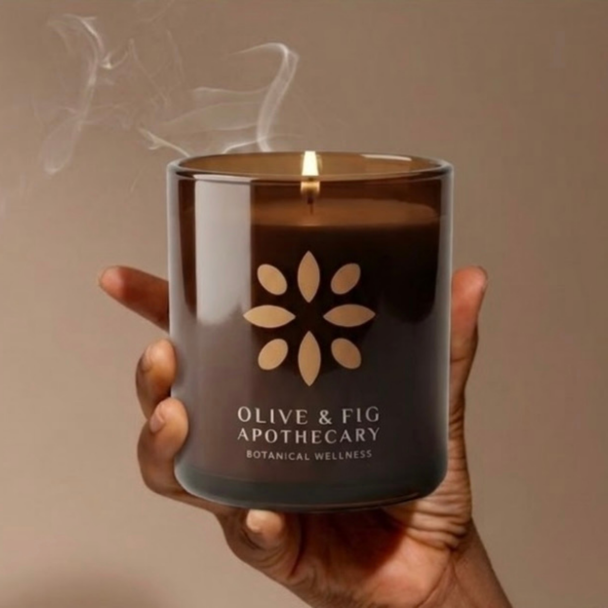 Hand holding an amber glass jar candle with floral emblem and lit wick