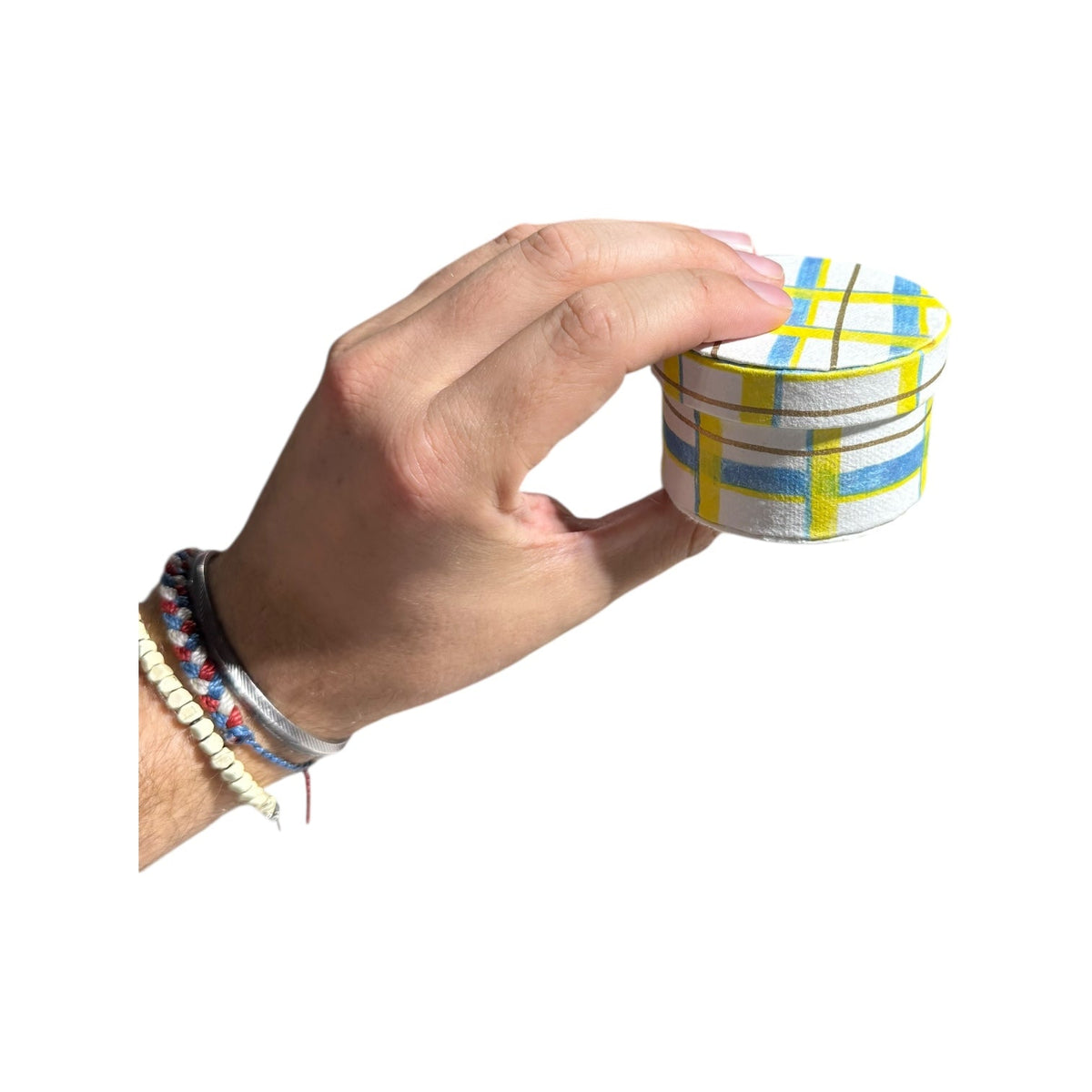 Hand holding a round handmade recycled paper gift box with blue and yellow plaid stripes.