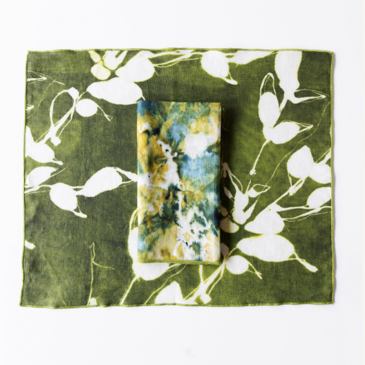 Olive green placemat with white floral vine pattern, small blue card centered