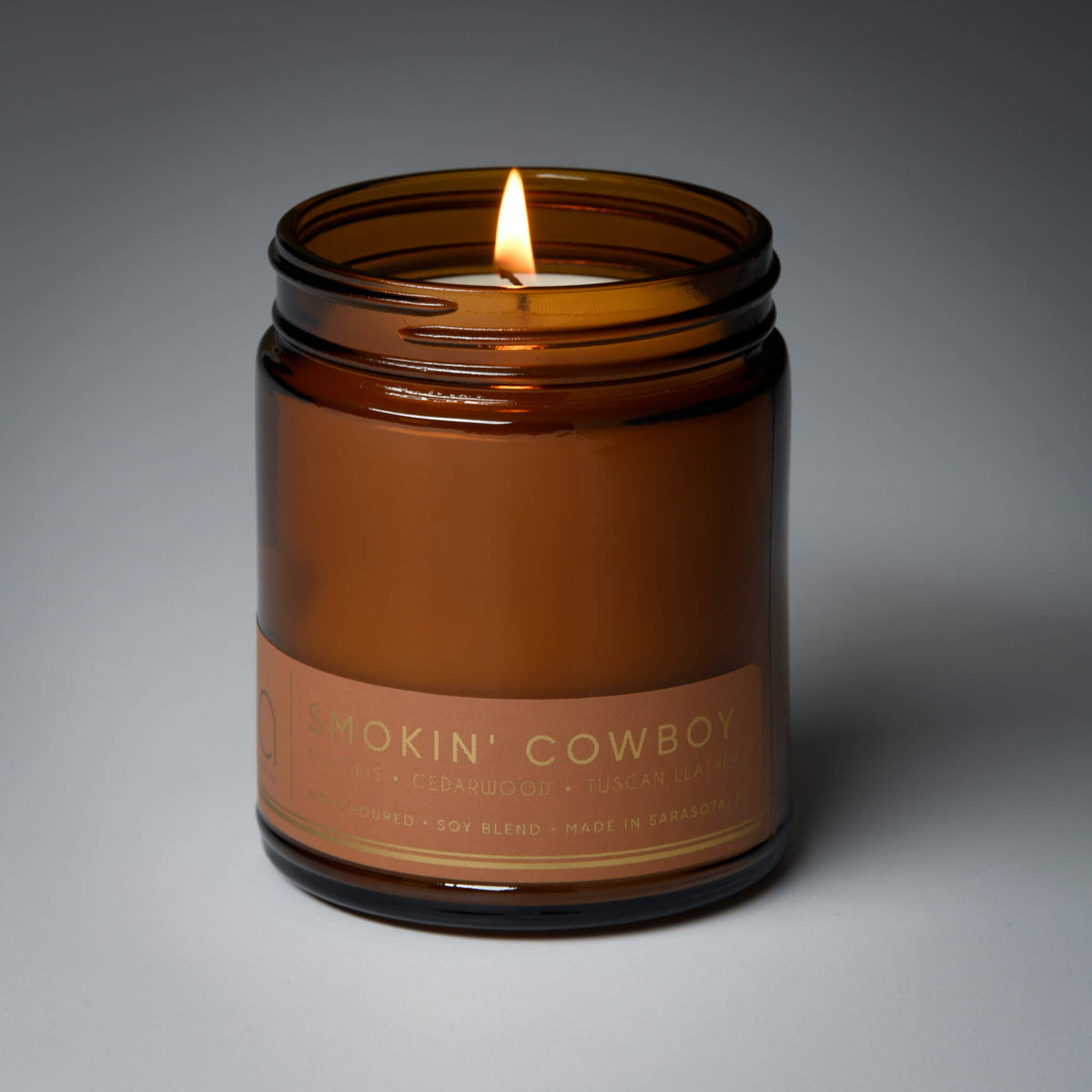 Amber glass candle jar with burning wick and 'Smokin' Cowboy' label