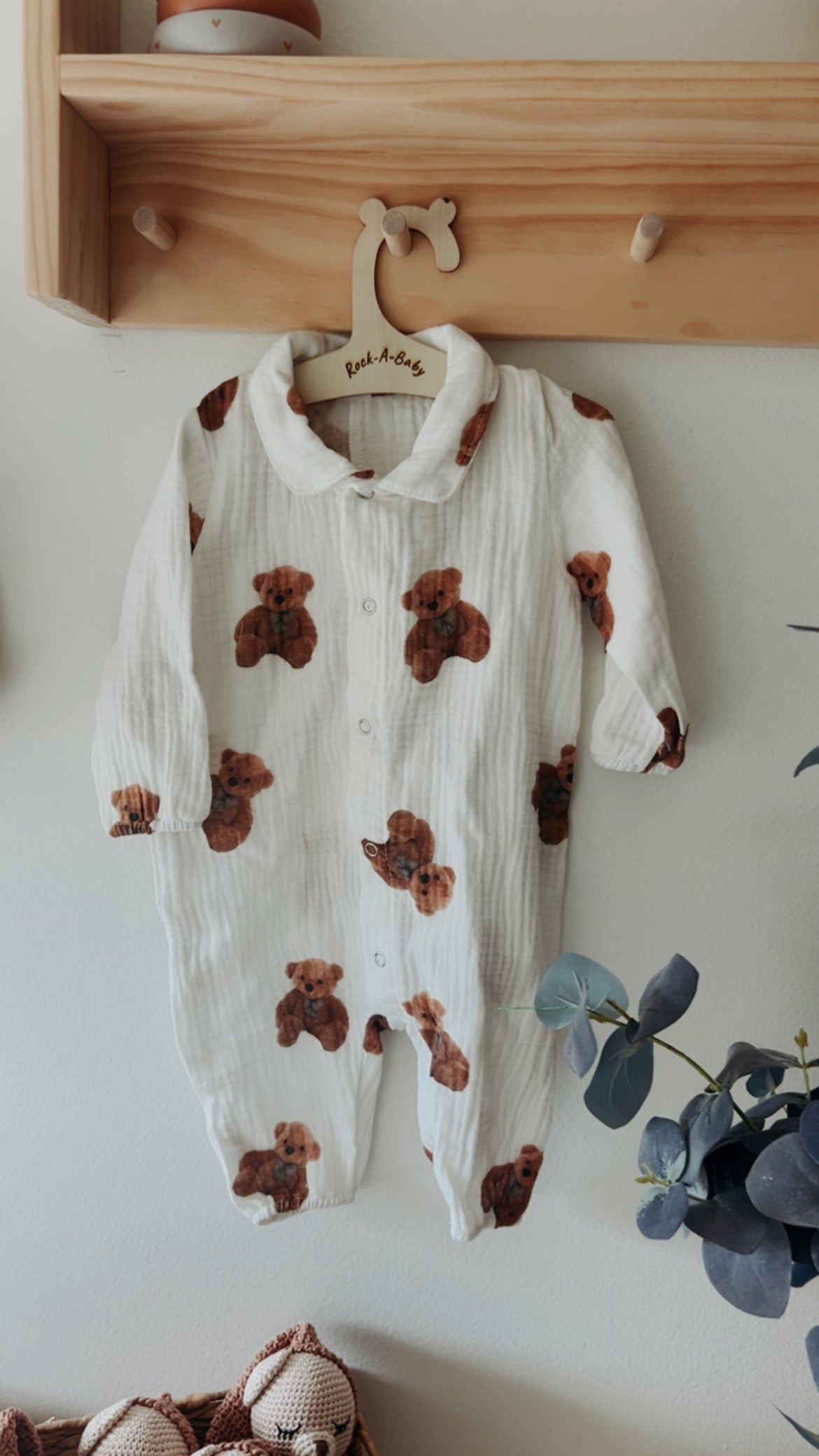 Bear-print baby romper with collar and button snaps on a wooden wall hanger