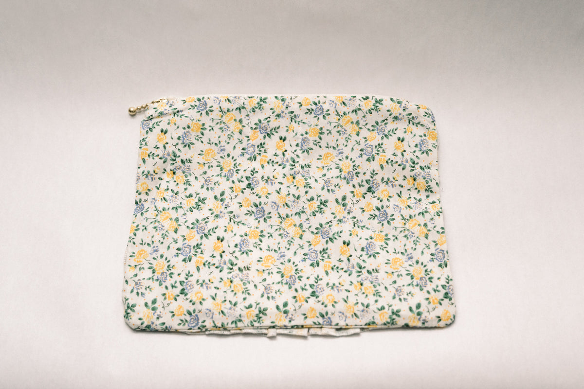Cream floral zipper pouch, flat top with gold zipper pull and gathered ruffle trim.