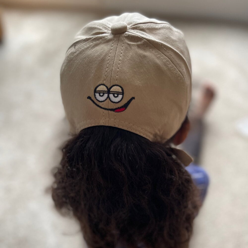 Kids baseball cap in light beige with a cartoon face and “m” logo