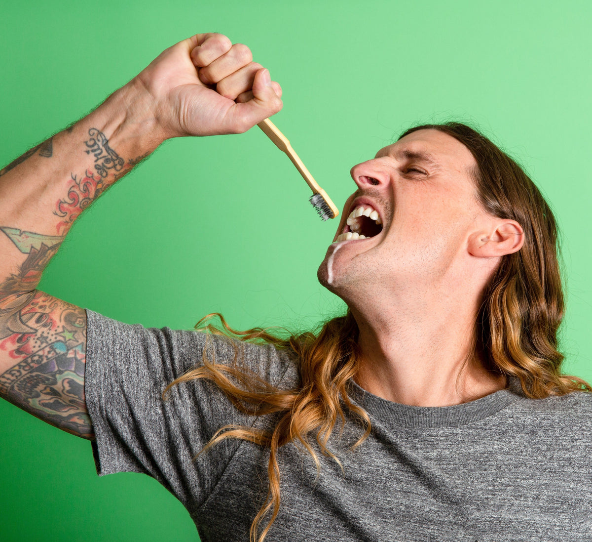 Bamboo toothbrush with toothpaste tablets being brushed on a person's teeth.