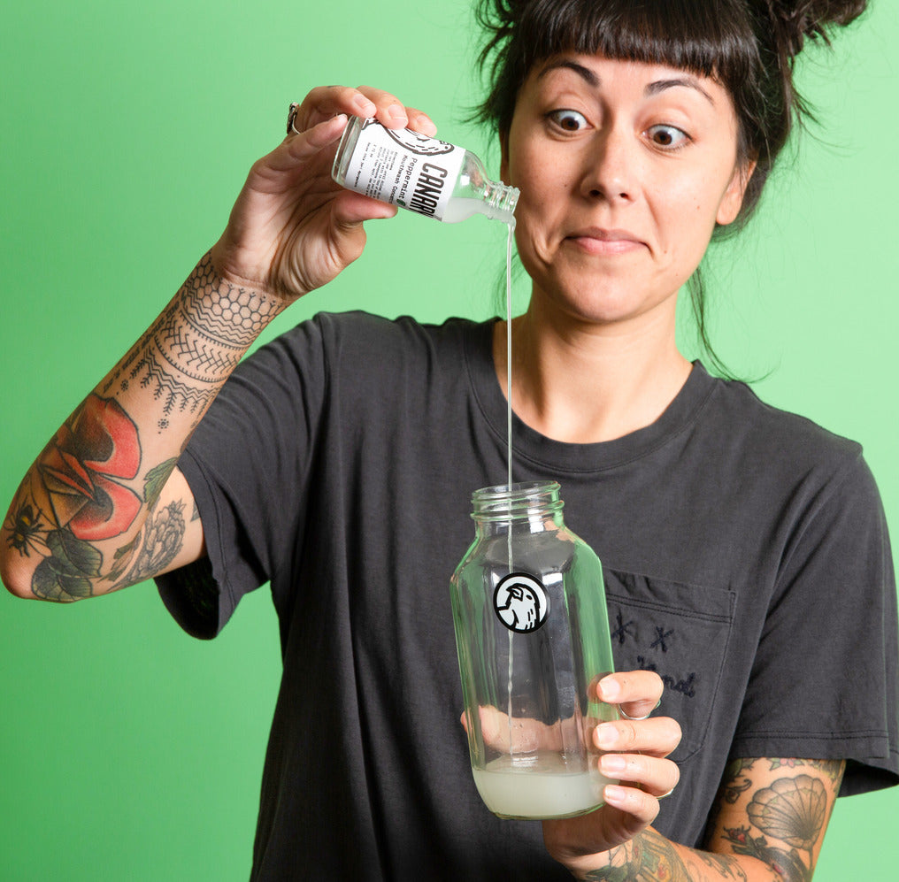 Peppermint mouthwash concentrate being poured from a small bottle into a glass jar