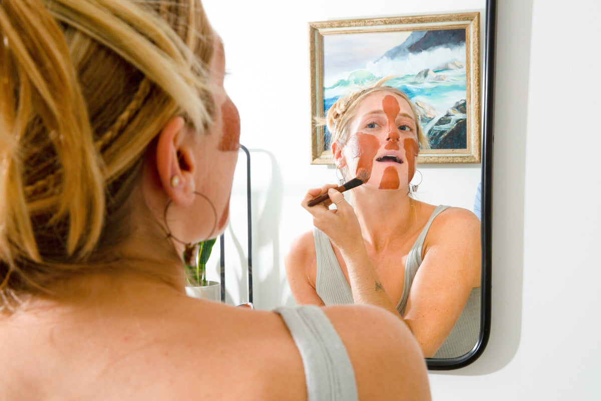 Rhassoul clay face mask being applied to a woman's cheek with a brush