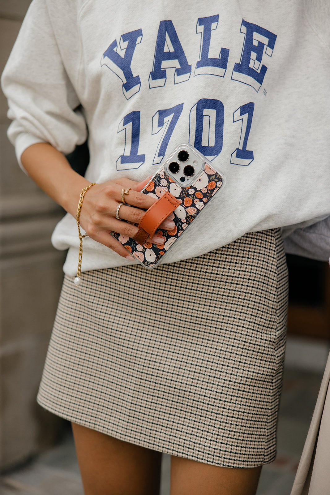 Floral phone case with brown strap, clipped to phone while wearing a varsity top