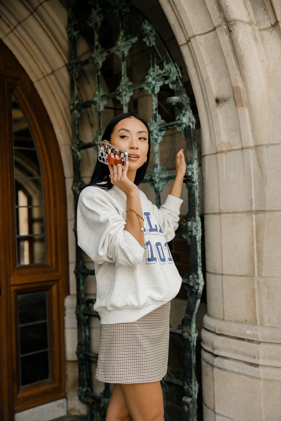 Floral phone case with brown strap, held in front of a white sweatshirt