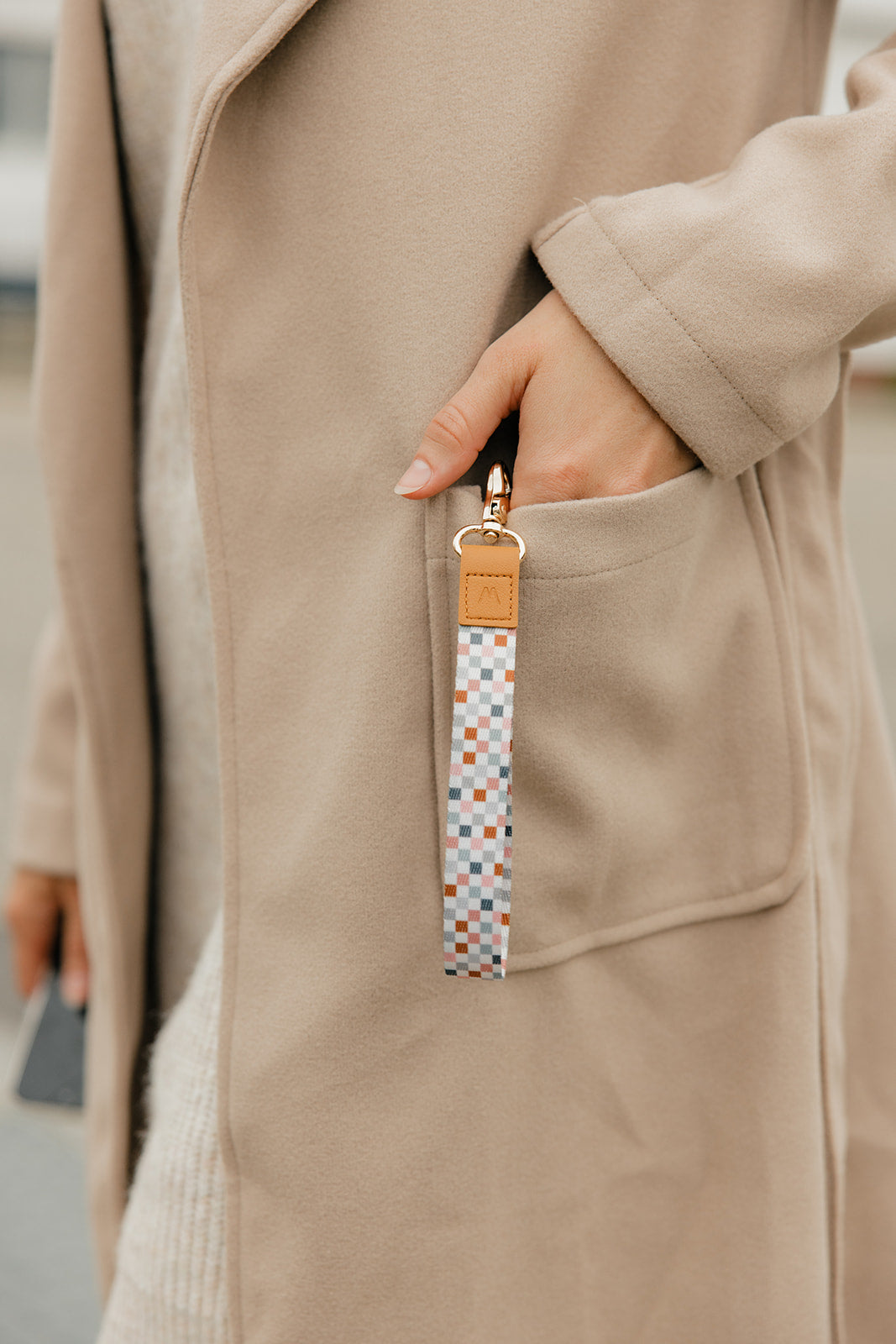 Check-pattern wrist lanyard with tan leather strap and gold clasp on wrist