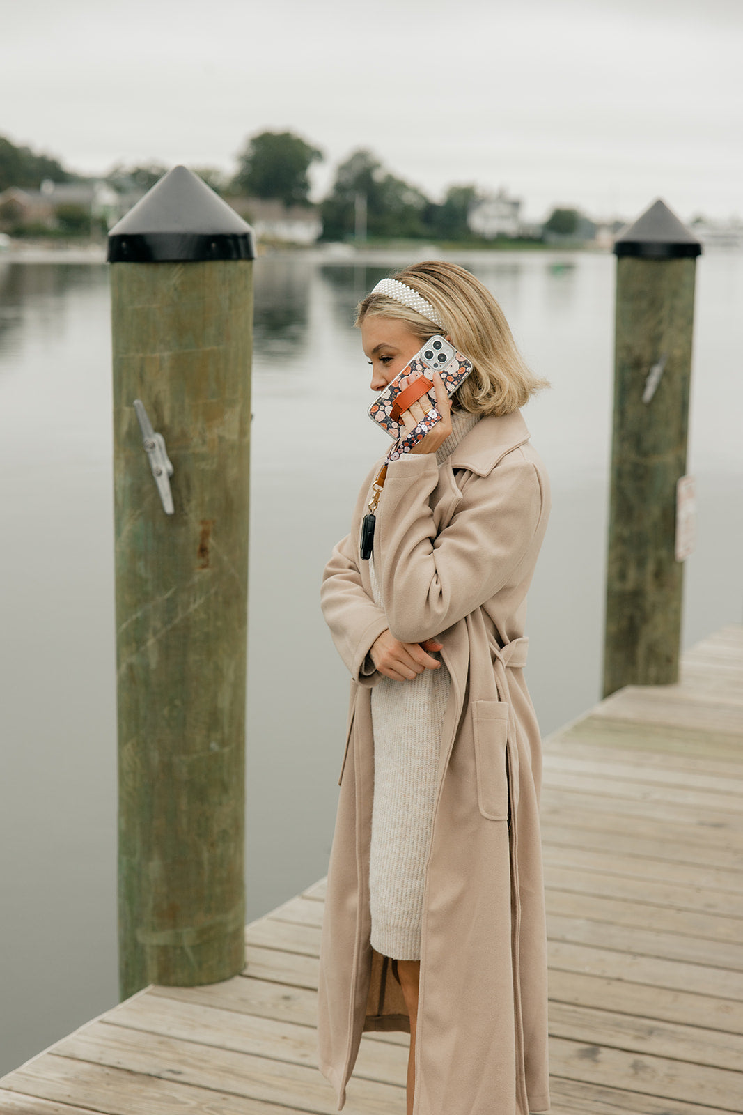 Phone case with floral print and brown strap, held against a beige coat