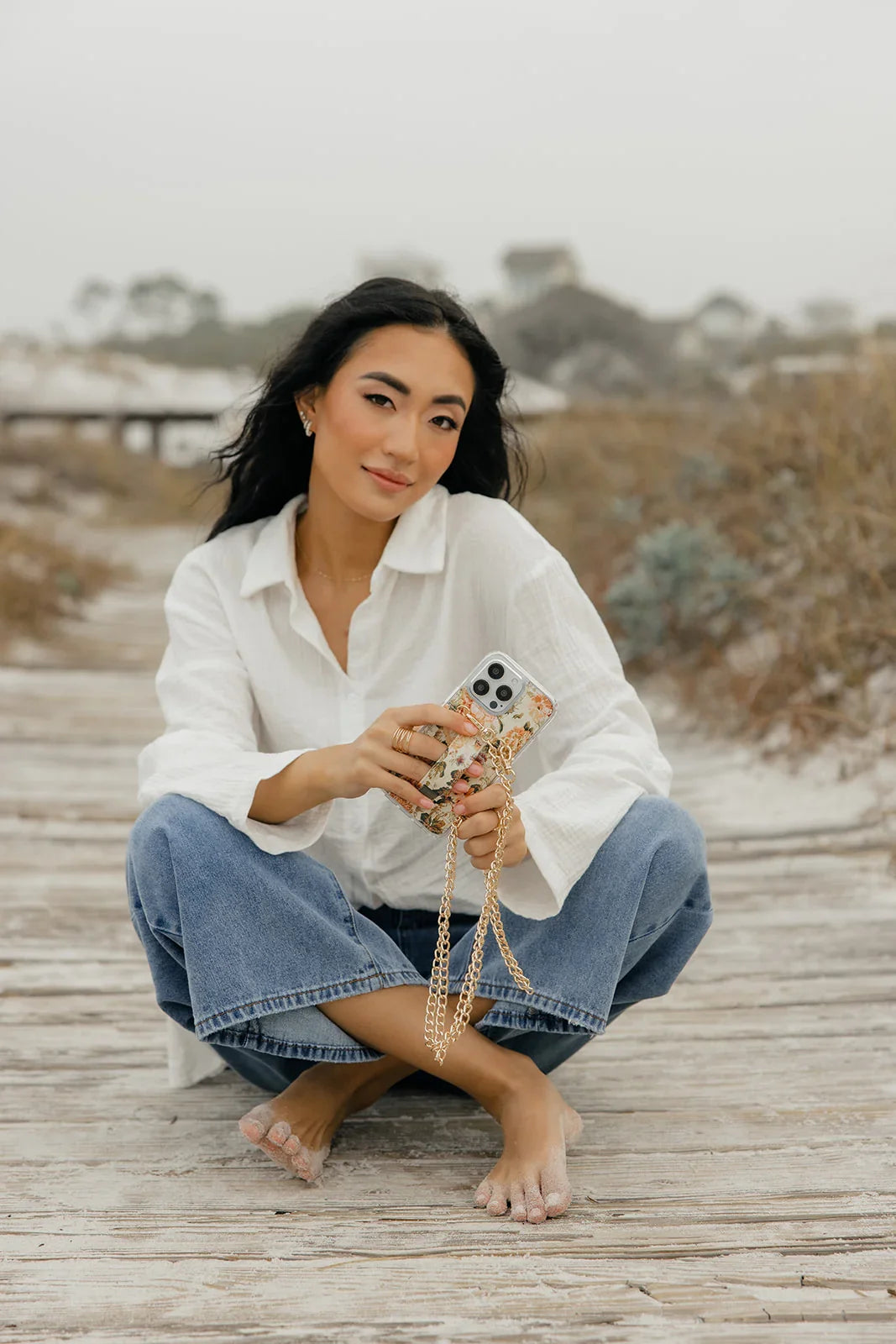Floral phone purse case with gold chain, held in hand over white shirt