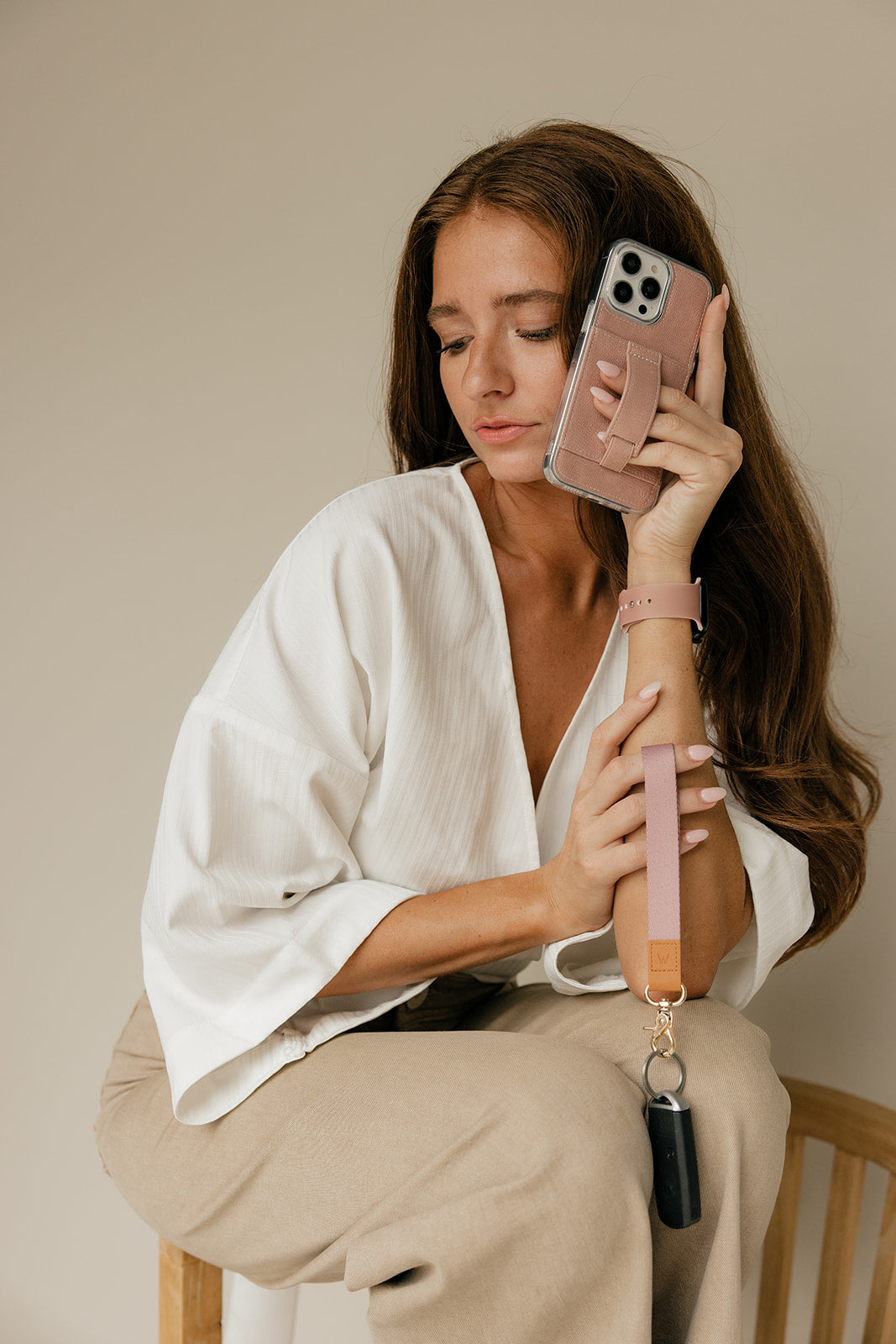 Pink wrist lanyard with tan leather tab and gold clip, worn while holding smartphone