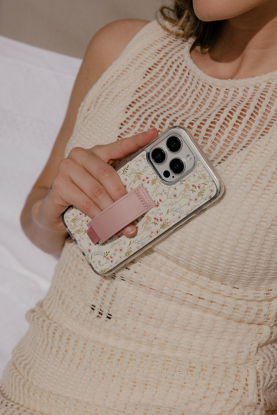 Floral clear phone case with mauve strap, held against a knit top; camera lenses visible