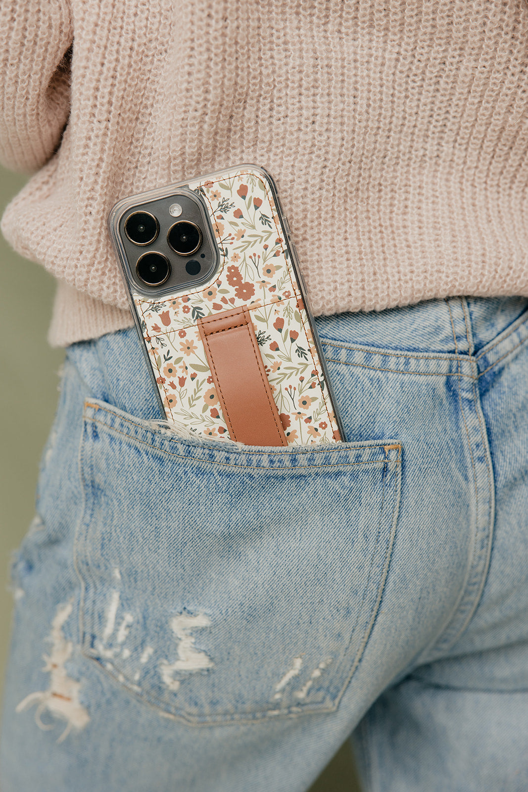 Floral phone case with brown strap pocket on smartphone over denim pocket