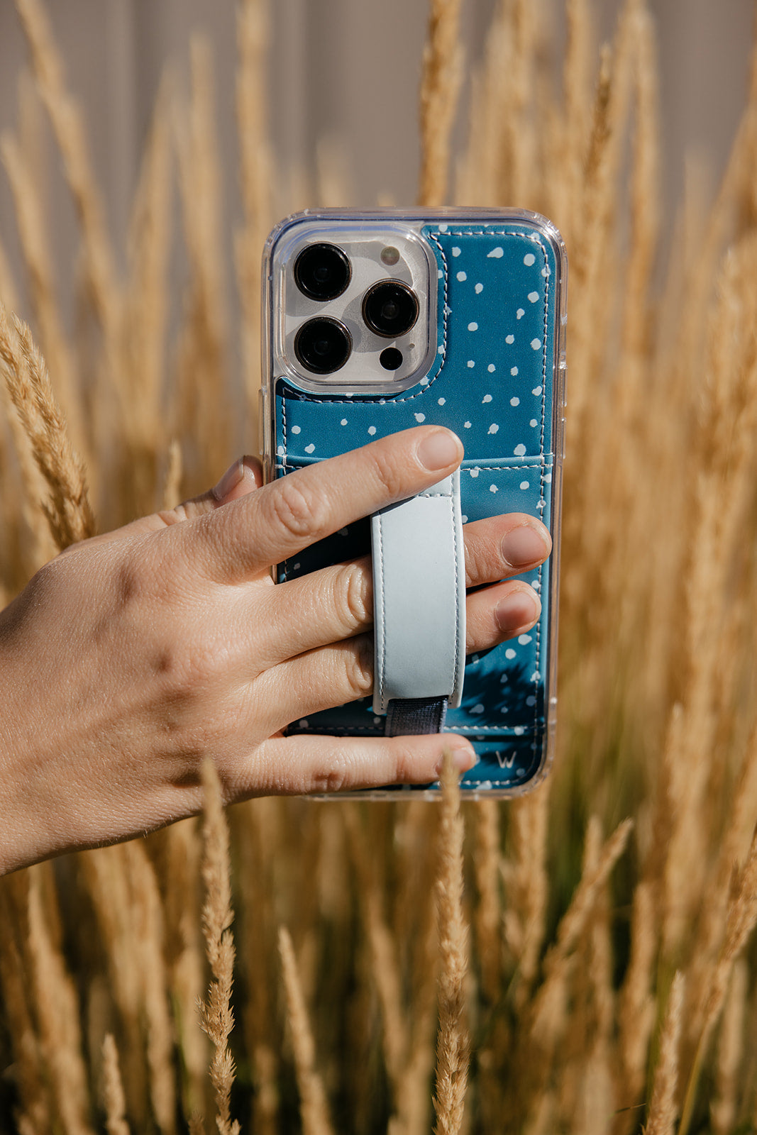 Teal phone case with white speckles and light strap holder, hand-held