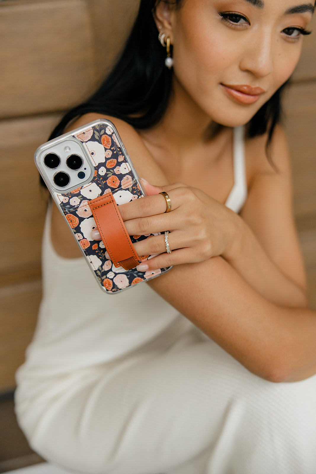 iPhone case with floral pattern and brown strap, shown in hand
