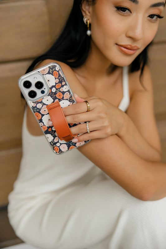 iPhone case with floral pattern and brown strap, shown in hand