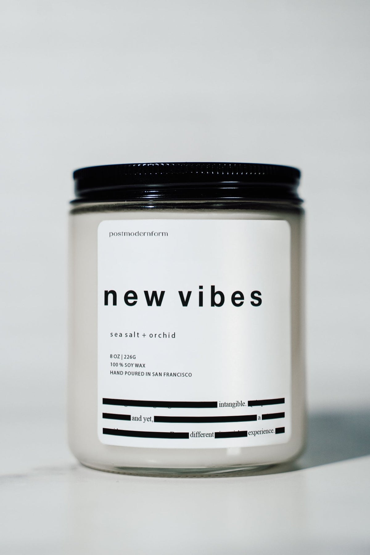 Candle jar with black lid and white label reading "new vibes" and "sea salt + orchid"