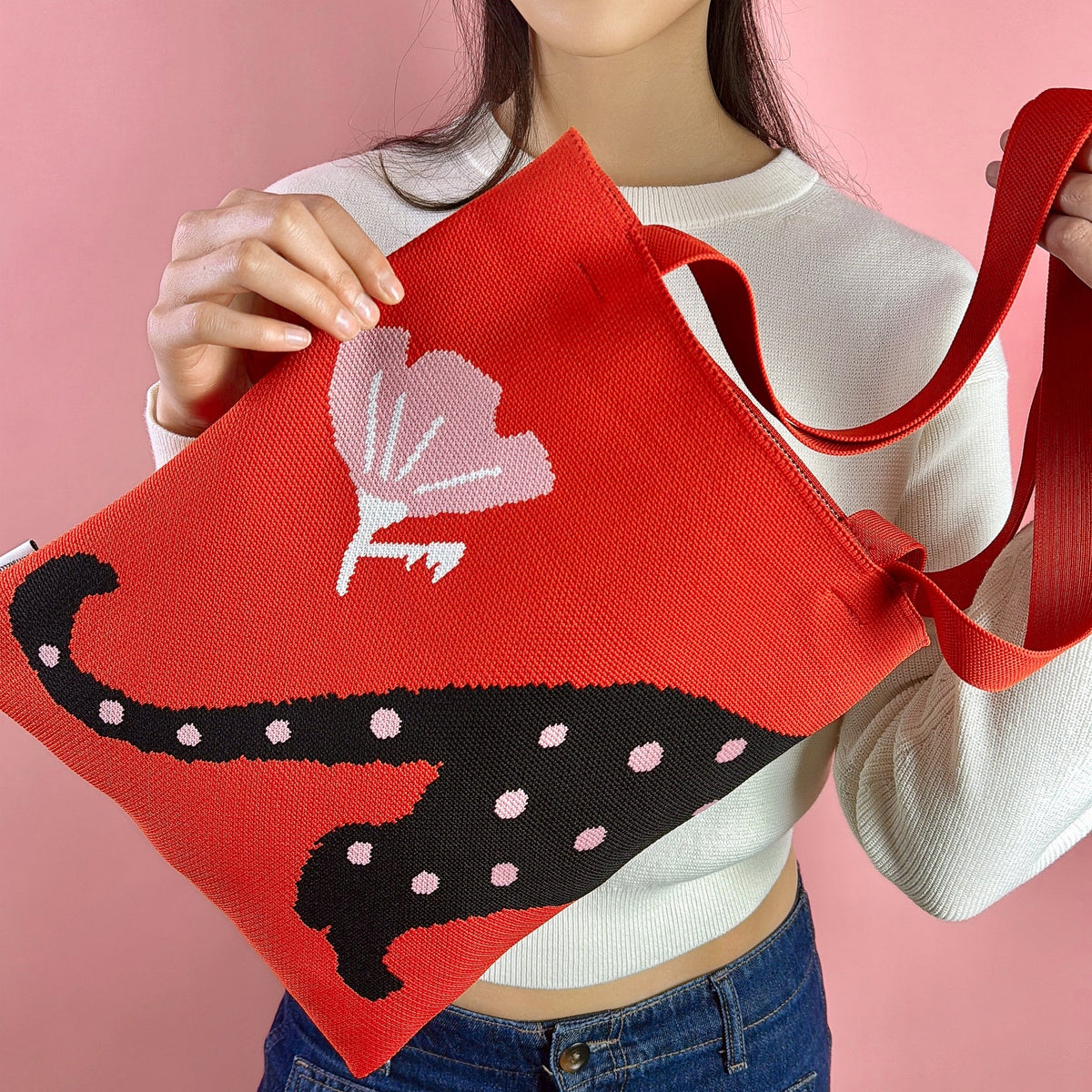 Red knit tote bag with black cat silhouette and white dot pattern, held forward.