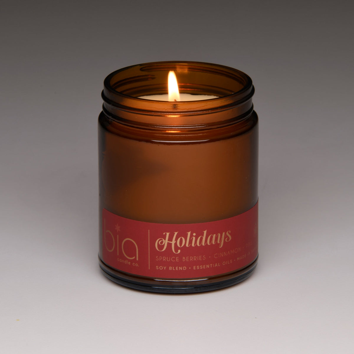 Amber soy candle jar with lid and lit wick, “Holidays” label centered