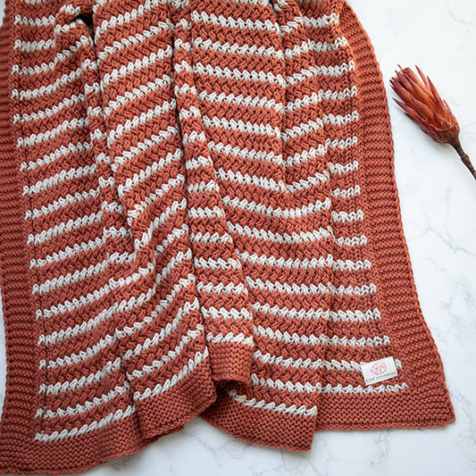 Rust and white striped knit throw blanket, stitched edge and woven brand tag