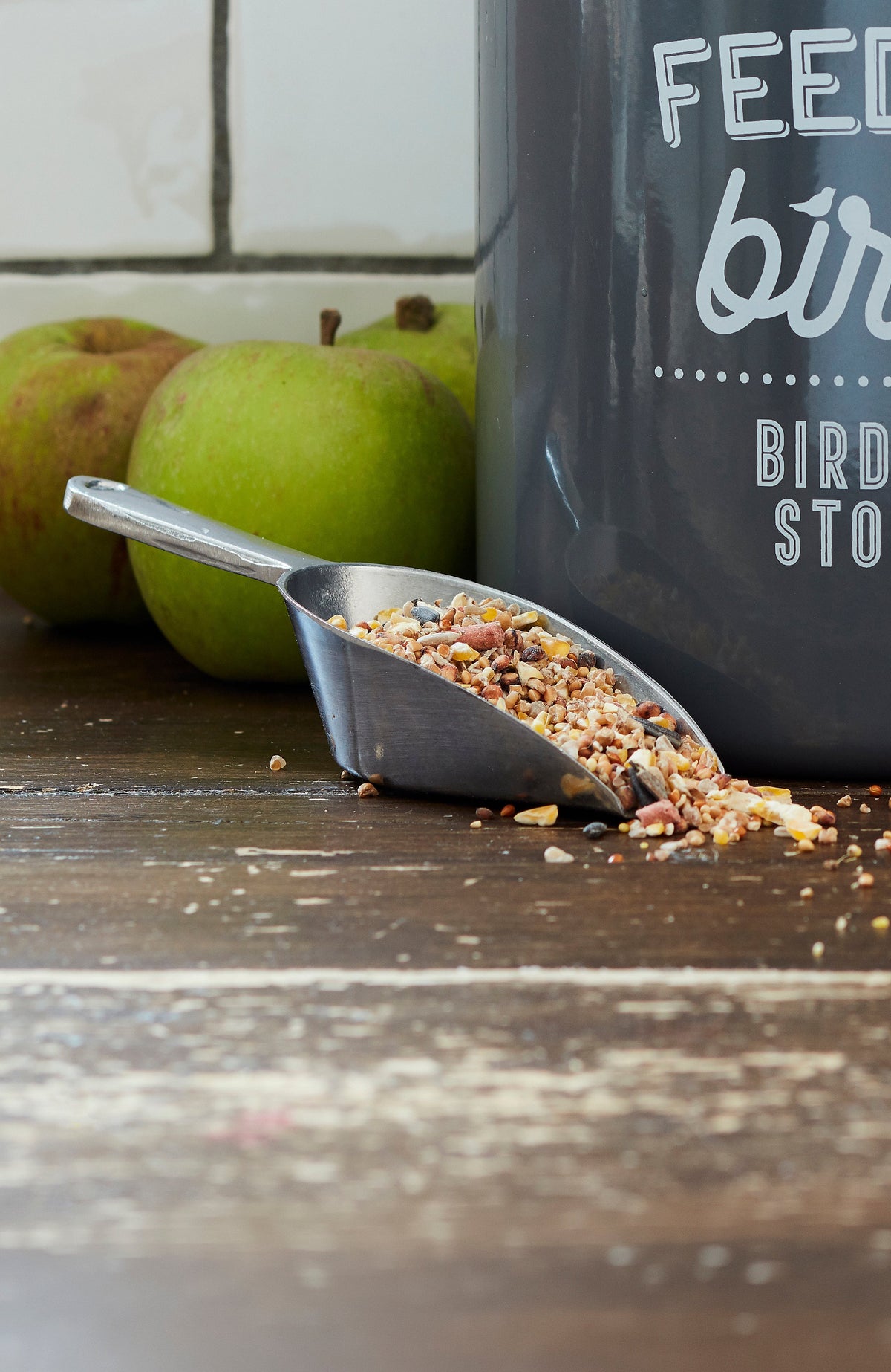 Charcoal bird feed storage tin with metal scoop and scattered seed feed