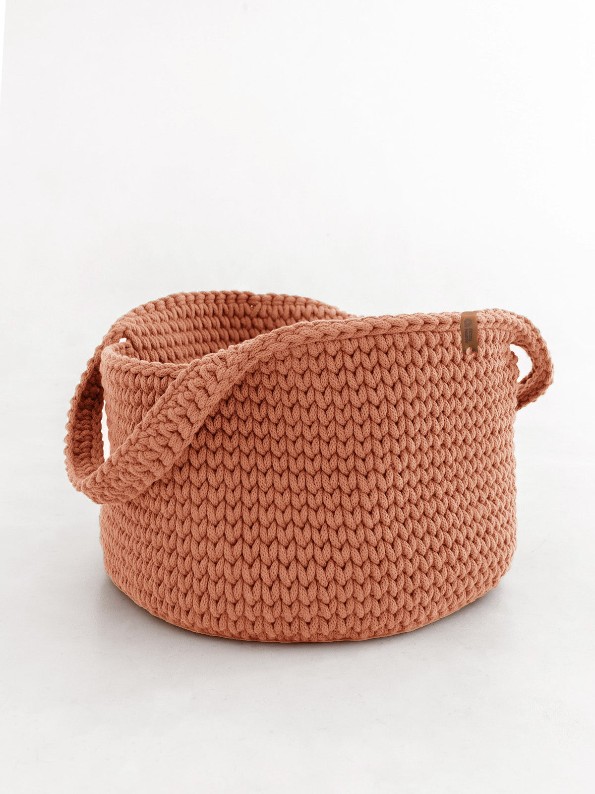 Round woven basket with handles, terracotta-coral knit texture.