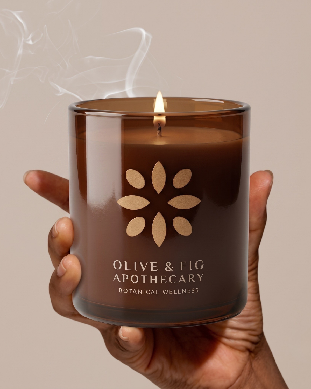 Lit amber glass jar candle with floral emblem, held by hands