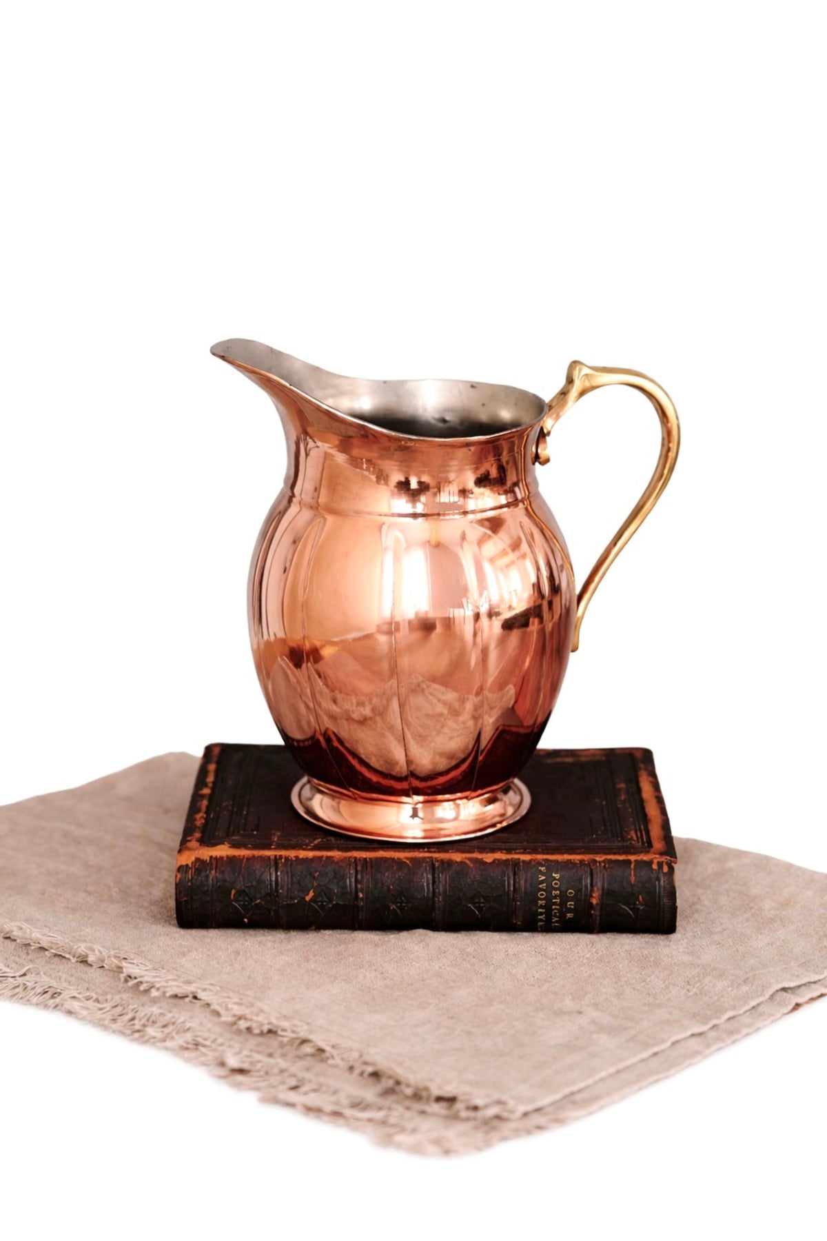 Copper metal pitcher with curved handle and flared spout, reflective rim.