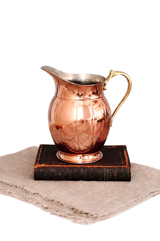Copper metal pitcher with curved handle and flared spout, reflective rim.