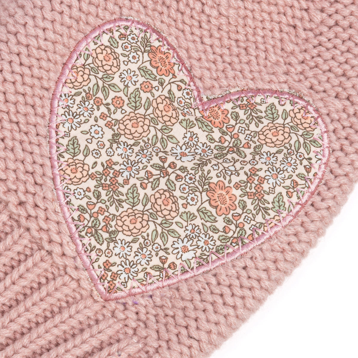 Close-up of the beanie's floral heart patch on pink knit fabric