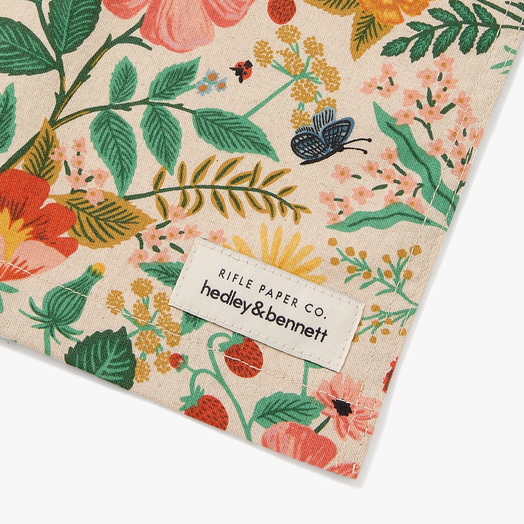 Floral apron with stitched brand label tag reading “Rifle Paper Co.”